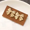 Pair of elegant gold-tone metallic bow-shaped stud earrings on a wooden display card - 3D Pleated Bowknot Stud Earring (N-356)