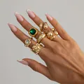 Set di anelli hip-hop dorati con pietre preziose verdi e trasparenti sulla mano. - Set di Anelli Hip Hop con Gemma Verde e Strass (07174) / Oro chiaro