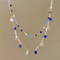 Close-up detail of a double-layered gold chain necklace with blue beads and crystal charms. - Double Layer Necklace / Aqua