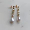 Dettaglio di eleganti orecchini pendenti con perle d'acqua dolce e perline placcate oro. - Taglia unica / Orecchini con perle di varie dimensioni e distanziatori dorati