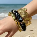 Exaggerated gold flower cuff and black acrylic beaded bracelet set worn on beach background - Black Acrylic and Gold Relief Flower 3-Piece Set (32669)