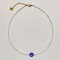 Detailed view of handmade white seed bead necklace featuring a blue glass evil eye charm. - Style Q / One Size / 38+5cm / White