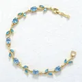 Elegant gold leaf branch bracelet with light blue gemstones on textured white background. - Gold Sky Blue Zirconia Tulip