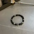 Elastisches Perlenarmband mit schwarz-weiß melierten Steinen und einem silbernen Kreuz - Schwarz-weißes Kreuzarmband mit Schneeflockenmuster / Schwarz und Weiß gemischt