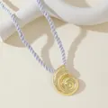 Détail macro d'un pendentif nautile doré associé à un cordon de soie torsadé violet - Collier Doré