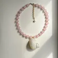 Close-up van roze kralenketting met een grote iriserende witte schelphanger aan de ketting. - Wulkhanger Ketting / 38+5cm / Roze ronde kraal