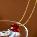Close-up of an irregular red crystal pendant on a gold chain with elegant lighting - Red