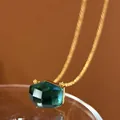Macro view of dark green irregular faceted crystal pendant on gold chain necklace - Ink Blue