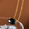 Detailed macro view of a dark green faceted crystal necklace with a minimalist gold chain. - Emerald