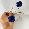 Nahaufnahme eines goldenen Armreifs mit zwei blauen Stoffrosen vor weißer Wand. - 33521-ab-dark blue-EP