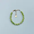 Gros plan détaillé d'un bracelet en pierres naturelles colorées avec un pendentif cœur - Style de perles rondes plates vert clair semi-transparentes / Taille unique / 17+3cm / Vert clair