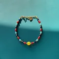Détail d'un bracelet en perles de pierres naturelles colorées avec un charme de cœur doré - Style de perles rondes rouge cyan bleu foncé et grosse perle jaune / Taille unique / 17+3cm / Coloré