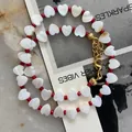 Detail view of heart-shaped shell beads and red accents on gold-plated necklace - Red Bead Heart Style / 38+5cm / Red