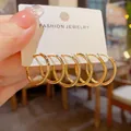 Set van drie paar elegante goudkleurige oorringen gepresenteerd op een sieradenkaart. - Gouden Creolen 3-delige Set