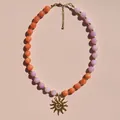 Primer plano de un collar con colgante de sol y cuentas color melocotón y lavanda - Estilo Colgante Sol de Cuentas Naranjas y Violetas
