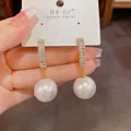 Gros plan détaillé de boucles d'oreilles dorées en C avec zircons et perles nacrées - Perle Blanche Forme C en Zircon (Plaqué Or Véritable)