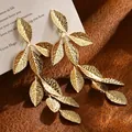 Close-up detail of golden textured leaf-shaped long drop earrings in vintage style - Leaf Tassel Stud Earrings / Gold