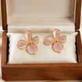 Elegant close-up of pink enamel cherry blossom stud earrings inside a wooden gift box. - Cherry Blossom Style / Pink