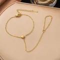 Close-up of a gold-plated stainless steel heart finger bracelet on a beige display - Mini Heart Hand Chain Bracelet (E2520)
