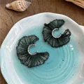 Primer plano de elegantes pendientes de abanico de malla verde oscuro en un plato de cerámica. - Estilo de Poste de Plata / Plateado-Verde
