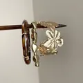 Vue détaillée d'un jonc doré à fleurs ajourées et d'un bracelet en résine écaille de tortue - Café / Ensemble trois pièces / Or