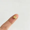 Kleiner goldener Muschel-Anhänger für DIY-Schmuck, auf einem Finger zum Größenvergleich - Muschel-Stil