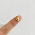 Makro-Detail eines goldenen Babyfuß-Edelstahlanhängers auf einem Finger zum Größenvergleich. - Babyfüße Stil