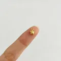 Makroansicht eines kleinen goldenen Sternanhängers auf einer Fingerspitze zur Größenangabe - Sternstil
