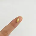 Detaillierte Makroansicht eines winzigen goldenen Schwammkürbis-Anhängers am Finger - Luffa-Stil