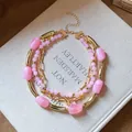 Exquisite detail of pink acrylic beaded layers and gold-toned chain necklace on a book - Pink / Gold