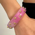 Close-up detail of a vintage pink acrylic wide bangle featuring elegant gold studs on a wrist - Pink With Dots (2722)