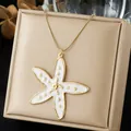 Detail view of a gold-plated starfish pendant necklace with white enamel on a gift box. - White Sea Star Enamel Gold Dot Style (N4556)