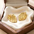 Detail of golden leaf-shaped stainless steel earrings on white silk in a wooden box - Texture Leaf