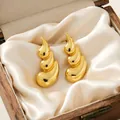 Close-up of polished gold spiral earrings resting on elegant white silk fabric - Water Drop Streamline