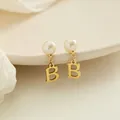 Elegante gouden pareloorbellen met een hangende letter B hanger getoond in een detailopname - Letter B