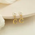 Macrodetail van elegante pareloorringen met een bungelende gouden hanger met de letter C - Letter C