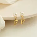 Orecchini a pendente con lettera F dorata e perla bianca su un espositore elegante - Lettera F