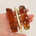 Tortoiseshell acrylic and gold metal cuff bracelets three-piece set held in hand - Amber Pattern Acrylic and Studded Metal 3-Piece Bangle Set (6787302) / Amber Set