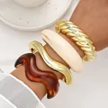 Stack of four statement chunky acrylic and gold-tone wave bracelets for women on wrist - Twisted Wave Bangle 4-Piece Set (6808301) / Set of 4 / Gold Cream Amber Combo