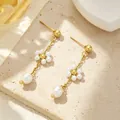 Gros plan sur des boucles d'oreilles plaquées or 18k avec fleurs délicates en perle - Boucles d'oreilles fleur en perles artificielles (E206) / Or