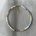 Bunte handgefertigte Natursteinperlenkette mit goldenem Herzanhänger auf grauem Hintergrund - Lila/Blau-Mix