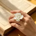 Primer plano detallado de un anillo de flor de resina blanca con perlas en un dedo. - Anillo de flor multicapa (WR1067) / Abierto Ajustable / Blanco