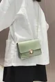 Detail van een mintgroene crossbodytas met ketting op een wit linnen overhemd. - Lichtgroen