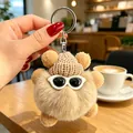 Primo piano di un simpatico portachiavi in peluche beige con cappello di lana e occhiali. - Ciondoli a pallina di fuliggine cachi