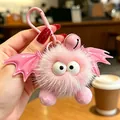 Primo piano di un portachiavi a mostro rosa peloso con ali di pipistrello e un campanellino rosa. - Diavolo Rosa