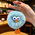 Primo piano di un simpatico portachiavi mostro di peluche azzurro tenuto in un caffè accogliente - Anatra carina azzurro chiaro