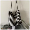 Vista detallada del bolso de lona a rayas blancas y negras en un entorno de estilo. - Bolso Tote de Hombro / Negro
