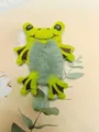Vista detallada de un lindo coletero de rana de peluche verde con textura de barriga gris - Rana