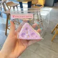 Λεπτομέρεια ενός μωβ παιχνιδιού squishy σε σχήμα βασκικού κέικ σε διαφανή συσκευασία - Τριγωνικό Τυρί / Μωβ