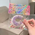 Detail shot of a purple donut-shaped TPR squishy toy in colorful retail packaging - Bitten Donut (White & Purple)